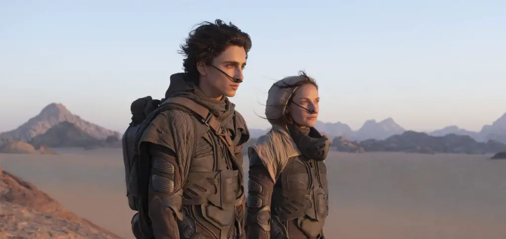 Paul Atreides (Timothée Chalamet) and Lady Jessica (Rebecca Ferguson), clad in stillsuits, survey the desert landscape of Arrakis in Denis Villeneuve's 'Dune' movie (2021).