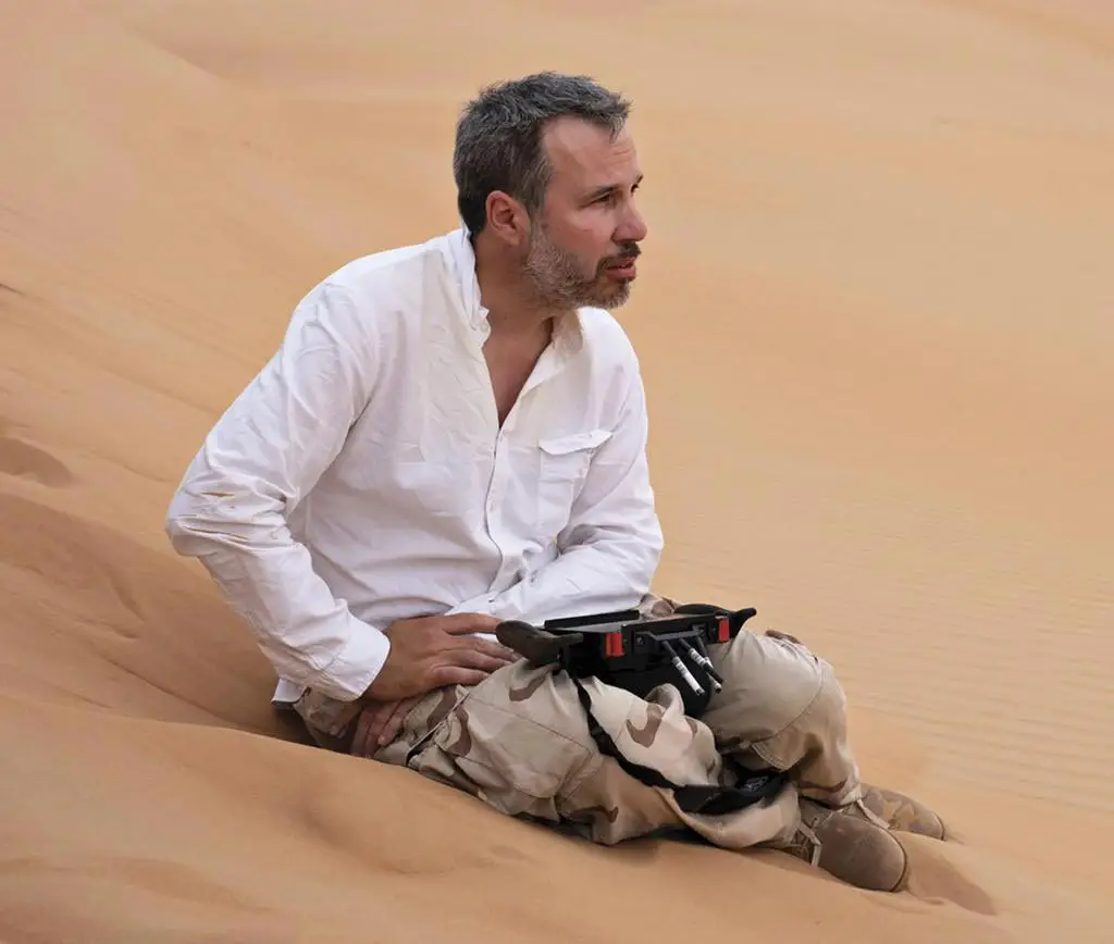 Close-up photo of Denis Villeneuve, sitting in the sands of the desert in Jordan, during production his 'Dune' (2021) movie.
