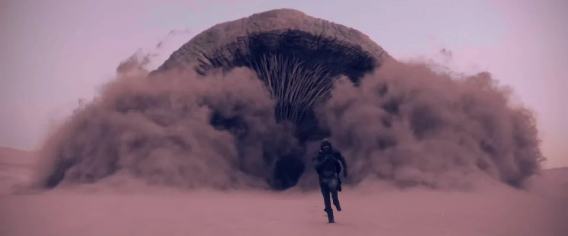 Paul Atreides runs from a gigantic sandworm in the Dune: Part One (2021) movie.