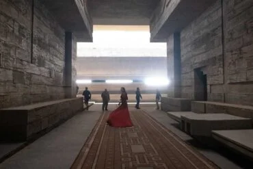 Behind-the-scenes photo from 'Dune' movie, featuring sets by production designer Patrice Vermette: Lady Jessica (Rebecca Ferguson), in red dress, walks through the Arrakeen residence.