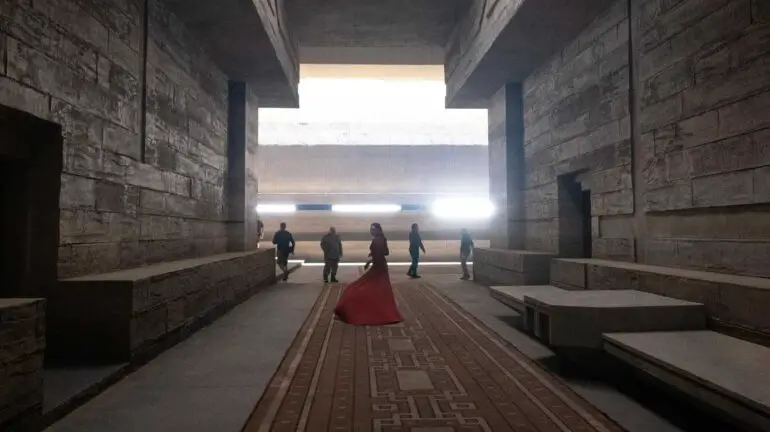 Behind-the-scenes photo from 'Dune' movie, featuring sets by production designer Patrice Vermette: Lady Jessica (Rebecca Ferguson), in red dress, walks through the Arrakeen residence.