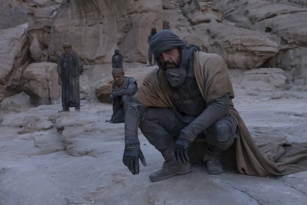 Stilgar squatting, with members of his tribe in background. The Fremen leader is played by Javier Bardem in Denis Villeneuve's 'Dune' movie adaptation. 