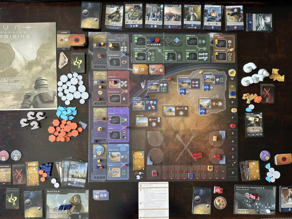 Photo of 'Dune: Imperium - Uprising' gameplay, showcasing board, card, tokens. and rulebook.
